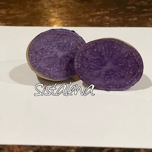 May include: Two halves of a purple potato, cut in half and showing the inside of the potato. The potato is a deep purple color and has a smooth texture.