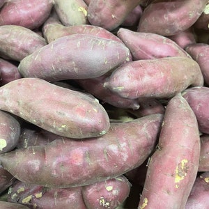 May include: A close-up of a pile of purple sweet potatoes. The potatoes are smooth and have a slightly rough texture.