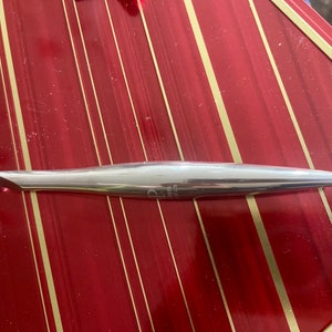 May include: A silver crochet hook with a size 5.5 mm marking. The hook is lying on a red and gold striped surface.