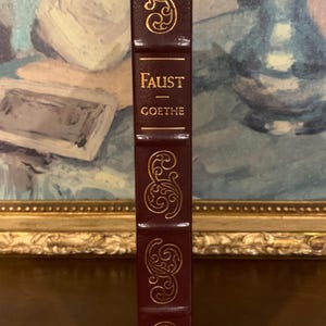 May include: A burgundy leather-bound book with gold lettering on the spine. The title is "FAUST - GOETHE".
