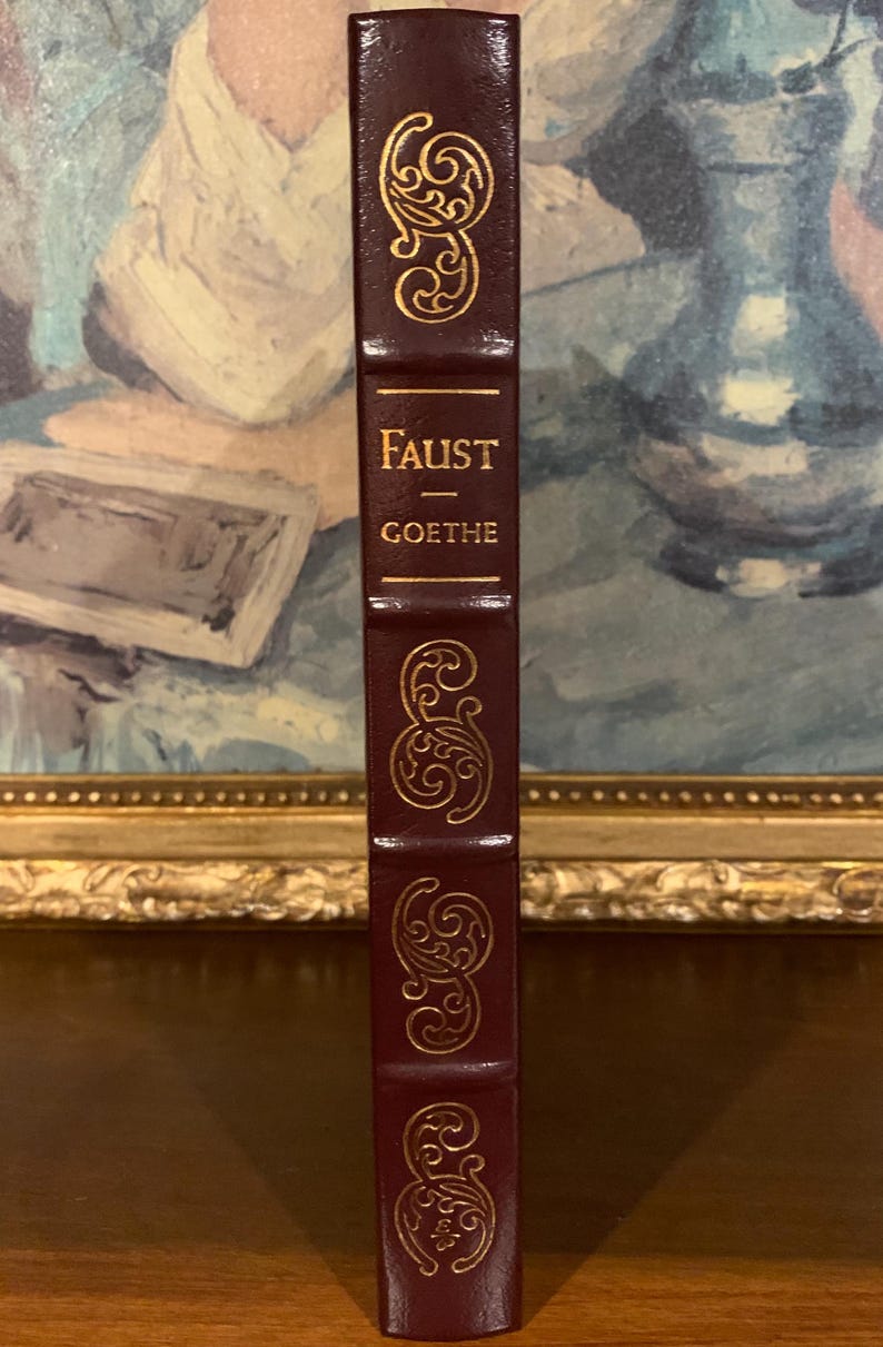 May include: A burgundy leather-bound book with gold lettering on the spine. The title is "FAUST - GOETHE".