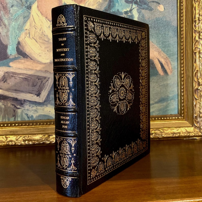 Vintage Leather-bound edition of “Tales of Mystery and Imagination” by Edgar Allan Poe with ornate gold detailing on the spine and cover. The book is displayed upright on a shelf.