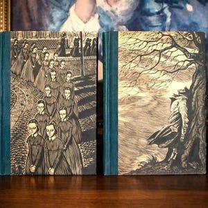 Peut inclure: Deux livres reli&eacute;s avec des dos bleu sarcelle fonc&eacute; et des couvertures cr&egrave;me orn&eacute;es d'illustrations &agrave; l'encre noire. Le livre de gauche montre une procession de filles en robe sur un chemin pav&eacute;. Celui de droite montre une personne adoss&eacute;e &agrave; un arbre.