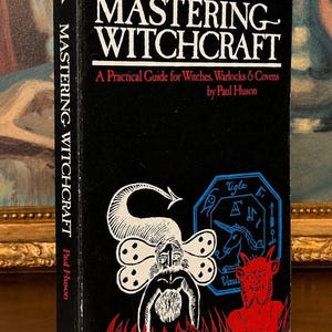 Puede incluir: Un libro de tapa dura negro titulado "Mastering Witchcraft" de Paul Huson. La portada presenta ilustraciones blancas y rojas de figuras y s&iacute;mbolos m&iacute;sticos. El lomo tambi&eacute;n muestra el t&iacute;tulo y el nombre del autor.