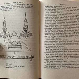 Puede incluir: Un libro abierto con texto e ilustraciones sobre brujer&iacute;a. La p&aacute;gina izquierda presenta un diagrama con velas, un tri&aacute;ngulo y una varita. La p&aacute;gina derecha contin&uacute;a con texto sobre adivinaci&oacute;n.