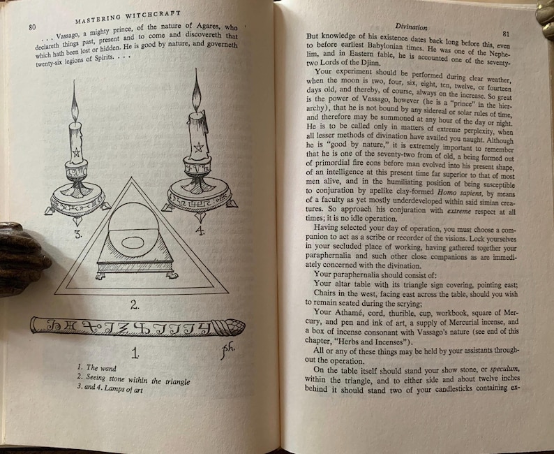 Puede incluir: Un libro abierto con texto e ilustraciones sobre brujer&iacute;a. La p&aacute;gina izquierda presenta un diagrama con velas, un tri&aacute;ngulo y una varita. La p&aacute;gina derecha contin&uacute;a con texto sobre adivinaci&oacute;n.