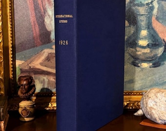 以下が含まれることがあります： 背表紙にInternational Studioという文字と1926年という数字が金色で印刷された、濃い青色のハードカバー本。本は垂直に立てられており、無地の布製カバーと、背表紙に記された明瞭で読みやすい金色の文字が特徴的です。