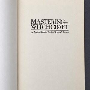 Puede incluir: P&aacute;gina de un libro abierto con el t&iacute;tulo "MASTERING WITCHCRAFT" en negro, con una fuente estilizada. Debajo, el subt&iacute;tulo dice "A Practical Guide for Witches, Warlocks & Covens". Las p&aacute;ginas son de color crema.