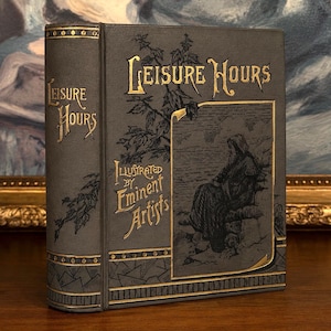 May include: A vintage book titled "Leisure Hours" with gold lettering and accents. The cover features an illustration of a seated figure and the text "Illustrated by Eminent Artists". The book has a dark gray cover.