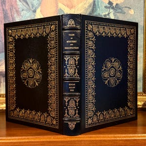 Vintage Leather-bound edition of “Tales of Mystery and Imagination” by Edgar Allan Poe with ornate gold detailing on the spine and cover. The book is displayed upright on a shelf.