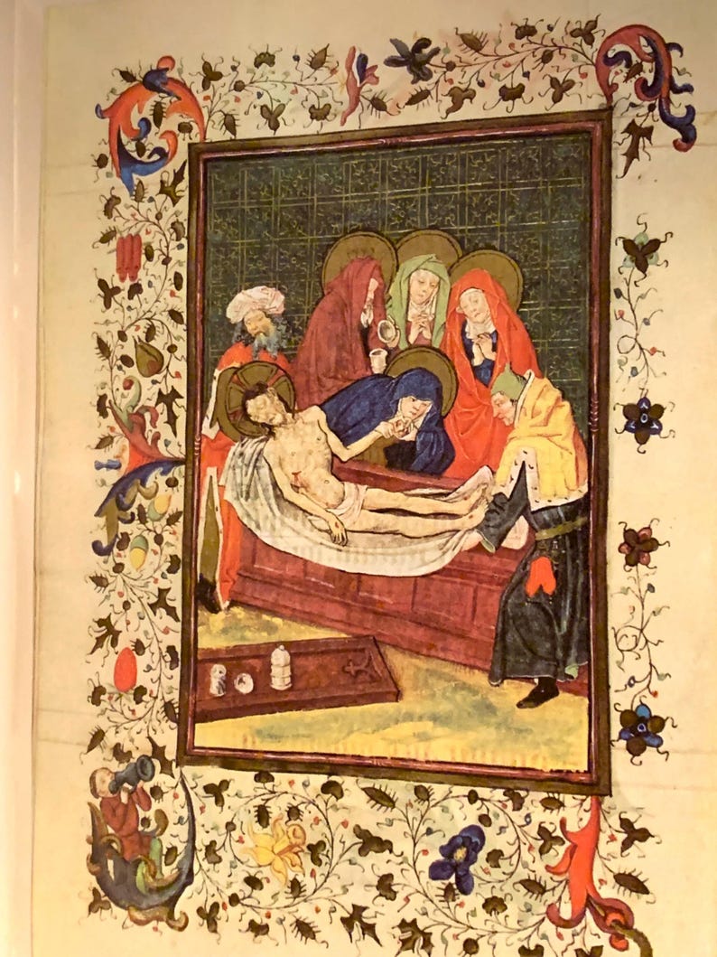 A medieval painting depicting the lamentation of Christ. The painting is framed in a gold frame with a decorative border of vines and flowers. The painting shows a group of people gathered around the body of Christ, who is lying on a wooden table. The people are dressed in colorful robes and are expressing their grief. The painting is done in a realistic style and is full of detail.