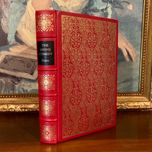 May include: A red leather-bound book with gold accents and the title "The Divine Comedy" by Dante.