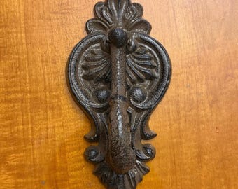 May include: Ornate, dark brown cast iron door knocker with a decorative floral design. The knocker features a central handle and a detailed, symmetrical pattern, perfect for adding a touch of vintage charm to any door.