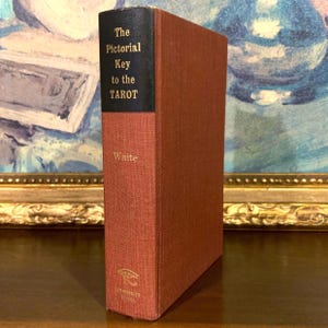 May include: A hardcover book titled "The Pictorial Key to the Tarot" by Waite. The book has a red cover with a black spine. The title and author's name are in gold lettering. The book is a vintage item.