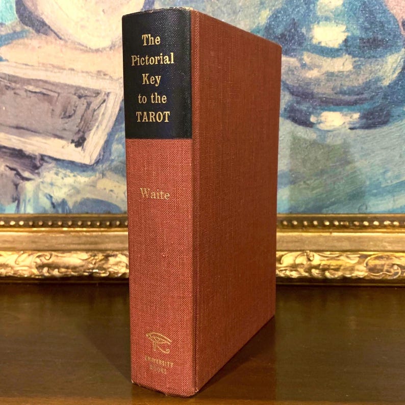 May include: A hardcover book titled "The Pictorial Key to the Tarot" by Waite. The book has a red cover with a black spine. The title and author's name are in gold lettering. The book is a vintage item.