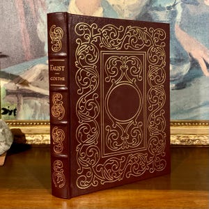 May include: A burgundy leather-bound book with gold embossed details and the title "FAUST - GOETHE" on the spine.