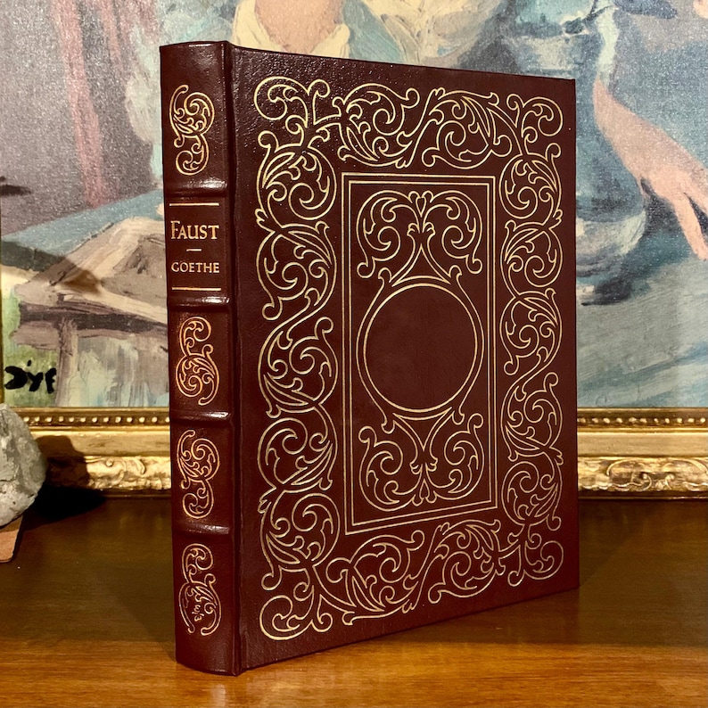 May include: A burgundy leather-bound book with gold embossed details and the title "FAUST - GOETHE" on the spine.