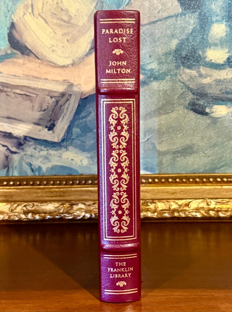Może przedstawiać: Burgundowa książka w sk&oacute;rzanej oprawie zatytułowana "Paradise Lost" autorstwa Johna Miltona. Grzbiet zdobią złote zdobienia i napis "The Franklin Library". Książka jest wyświetlana pionowo.