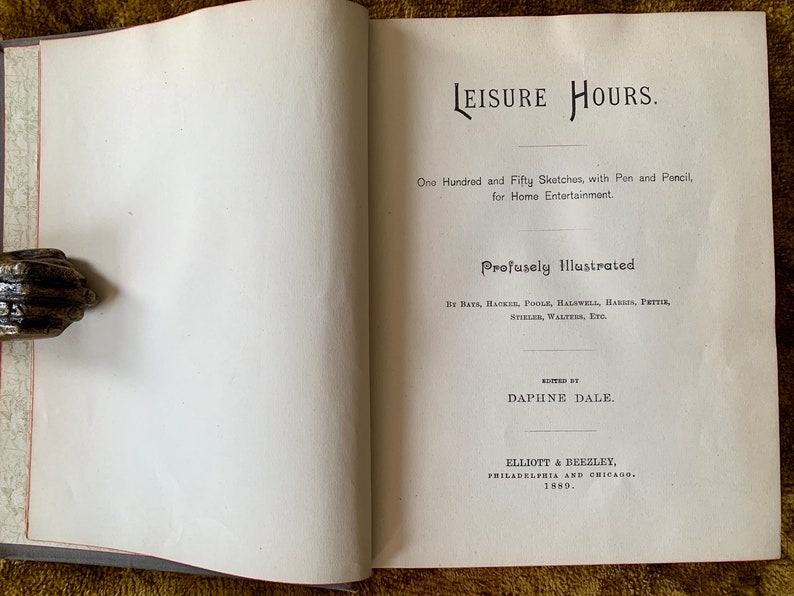 May include: Open book titled "LEISURE HOURS" with text and illustrations. The book is open to a page with text, including the title and author's name. A decorative metal hand holds the book open.