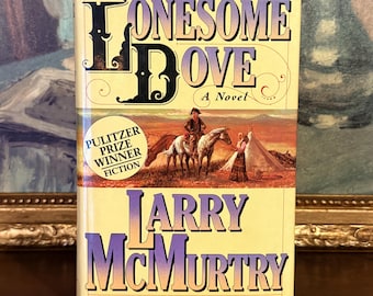 May include: A hardcover book titled Lonesome Dove by Larry McMurtry with a cream-colored cover. The front features a western illustration of a person on horseback and a person standing near a tent. A circular yellow sticker reads Pulitzer Prize Winner Fiction.