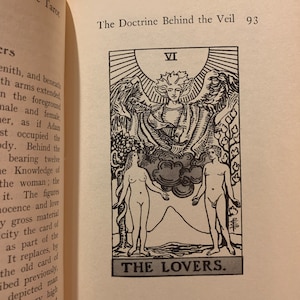 May include: An illustration of a tarot card titled "The Lovers" from a book. The card features two nude figures, a man and a woman, with a winged figure above them. The card is numbered VI.