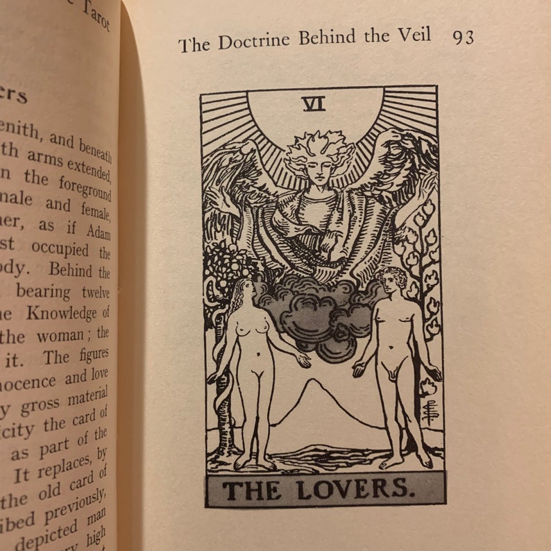 May include: An illustration of a tarot card titled "The Lovers" from a book. The card features two nude figures, a man and a woman, with a winged figure above them. The card is numbered VI.