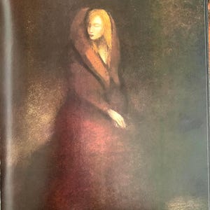 May include: A woman in a long, burgundy dress with a fur-trimmed hood sits in a dimly lit room. Her blonde hair is visible beneath the hood, and she has a soft, contemplative expression on her face.