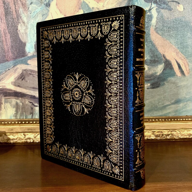 Vintage Leather-bound edition of “Tales of Mystery and Imagination” by Edgar Allan Poe with ornate gold detailing on the spine and back cover. The book is displayed upright on a shelf.
