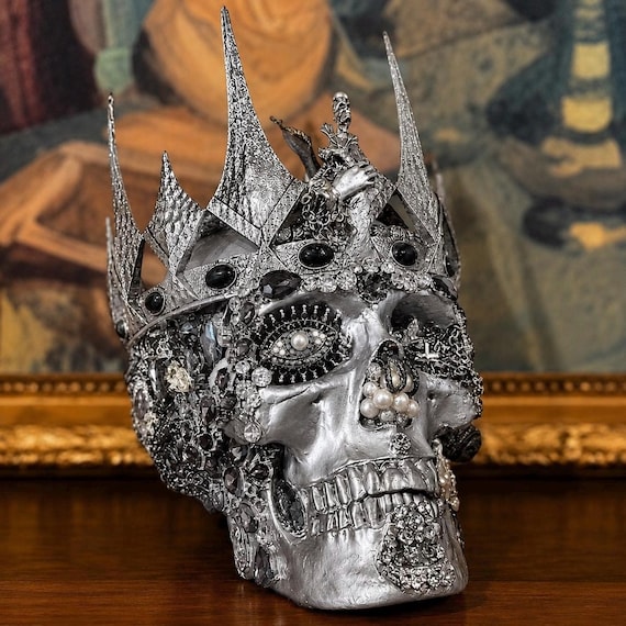 A handmade silver-toned skull crowned and encrusted with jewels — maximalist macabre royalty that looks like it belongs in a collector's cabinet.