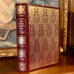 May include: A red leather-bound book with gold embossed details and the title "The Divine Comedy" by Dante.