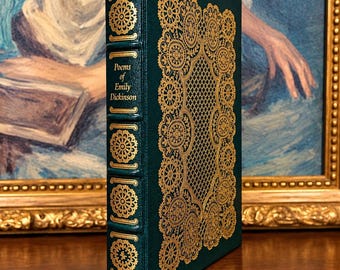 May include: A dark green hardcover book titled Poems of Emily Dickinson with gold foil stamping on the spine and front cover. The cover features an intricate gold lace-like pattern and a diamond grid design, while the spine has raised bands.