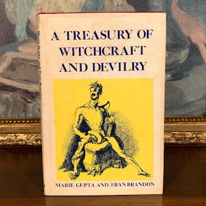 A vintage book titled "A Treasury of Witchcraft and Devilry" with a yellow and black illustration on the cover. The book's title is in blue text, and the author's names are at the bottom. The book is on a wooden surface.