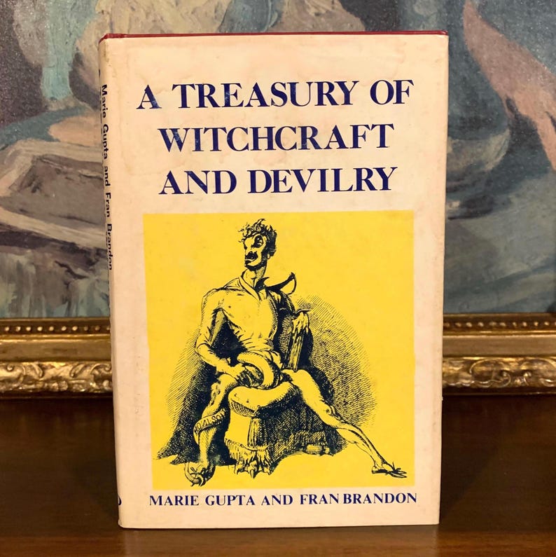 A vintage book titled "A Treasury of Witchcraft and Devilry" with a yellow and black illustration on the cover. The book's title is in blue text, and the author's names are at the bottom. The book is on a wooden surface.