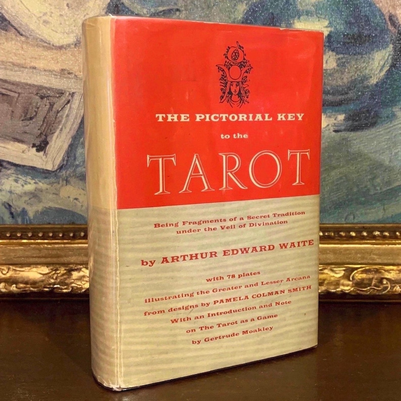 May include: A vintage book titled "THE PICTORIAL KEY to the TAROT" with a red and cream cover. The book features text by Arthur Edward Waite and illustrations by Pamela Colman Smith. The book is a guide to tarot divination.