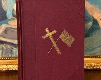 May include: A burgundy-colored book with a gold cross and American flag emblem. The cover has a textured appearance and a vertical orientation. The book's spine is visible on the left side, and the cover design is centered.