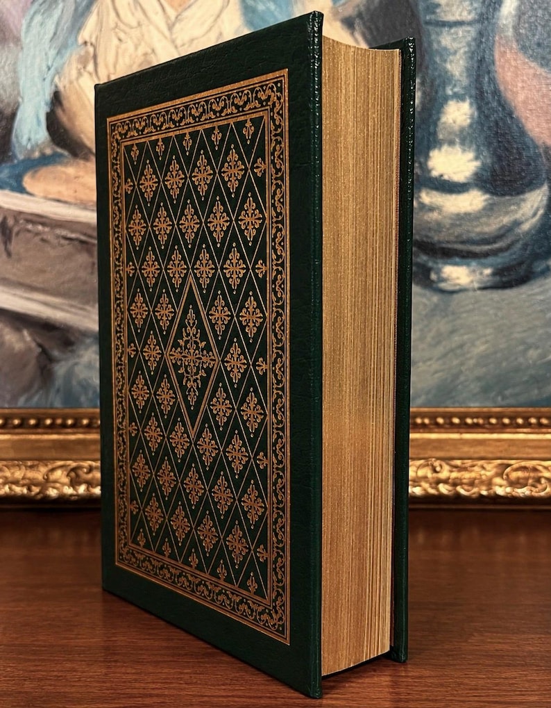 Vintage Leather-bound edition of The Poetry of Robert Frost in dark green with ornate gold gilt decoration on the cover, standing upright on a wooden surface in front of a framed painting.