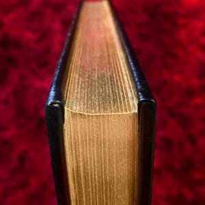 May include: Close-up of the spine of a hardcover book with gold-colored pages and a black cover.