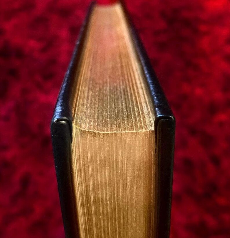 May include: Close-up of the spine of a hardcover book with gold-colored pages and a black cover.