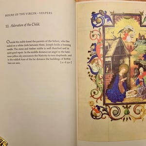 A medieval illuminated manuscript page with a depiction of the Nativity. The scene is set in a stable with a thatched roof. Mary kneels in a blue robe, holding the baby Jesus. Joseph stands behind her in a red robe. An angel with wings appears above the stable in a yellow sky. The text on the page reads 'HOURS OF THE VIRGIN-VESPERS 12. Adoration of the Child.