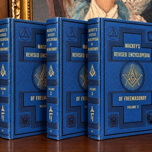 Könnte beinhalten: Drei blaue Hardcover-Bücher mit dem Titel Mackey's Revised Encyclopedia of Freemasonry, beschriftet als Band 1, Band 2 und Band 3. Jedes Buch zeigt goldgeprägten Text sowie ein Winkel- und Zirkelsymbol auf dem Einband und dem Buchrücken.