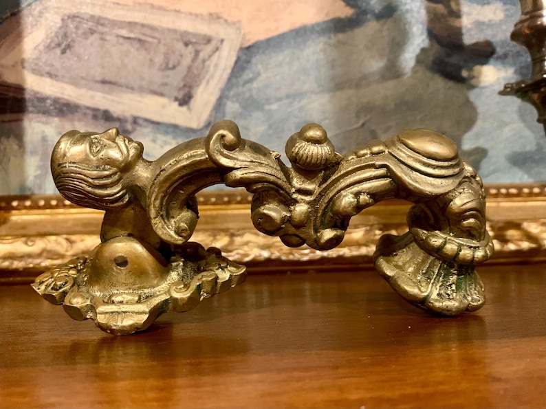 May include: Ornate brass furniture hardware with a detailed, sculpted design. The piece features a classical motif with a human face and scrolling embellishments. The hardware is likely for a drawer or cabinet, adding a touch of vintage elegance.