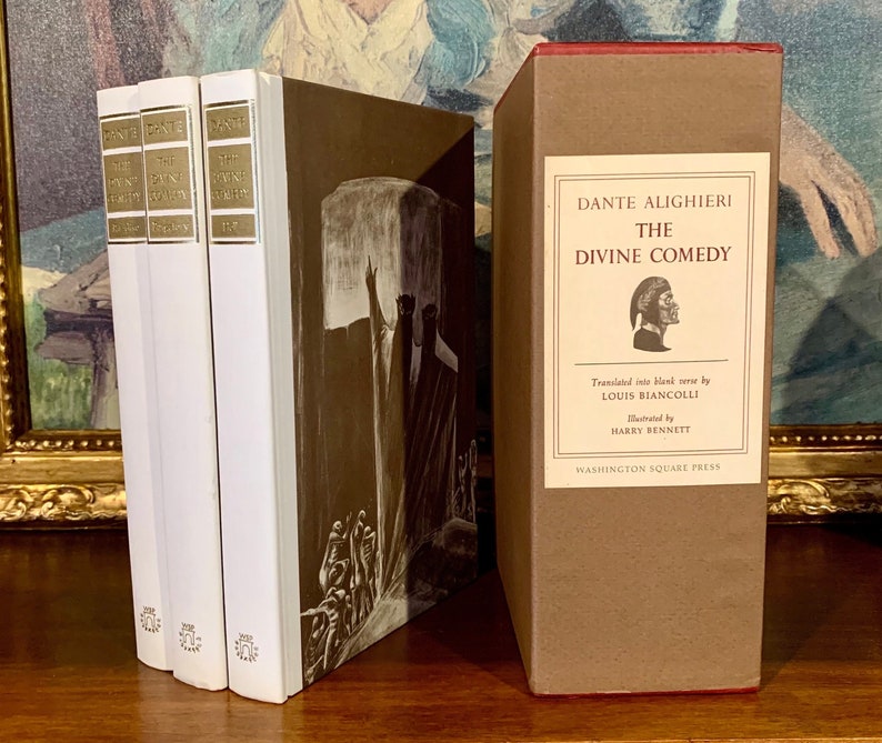 May include: A three-volume set of "The Divine Comedy" by Dante Alighieri, with a brown cover and white spines. The books are illustrated with a black and white drawing of a man in a robe, pointing upwards.