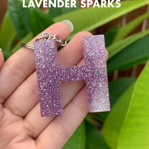 May include: A silver key chain with a sparkly lavender letter H charm. The charm is made of resin and has a glittery finish.