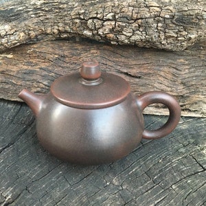 May include: A dark brown ceramic teapot with a rounded body and a small spout. The teapot has a handle on the side and a lid on top.