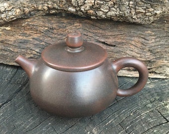 May include: A dark brown ceramic teapot with a rounded body and a small spout. The teapot has a handle on the side and a lid on top.