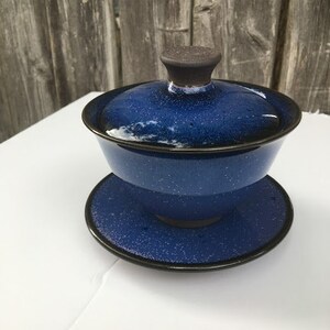 Könnte beinhalten: Ein blaues Keramik-Teekannen-Set mit dunkelblauer Glasur und einer gesprenkelten Oberfläche. Der Deckel hat einen dunkelbraunen Knopf.