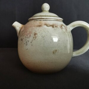 May include: A ceramic teapot with a light green glaze and brown speckles. The teapot has a round body and a lid with a knob on top.