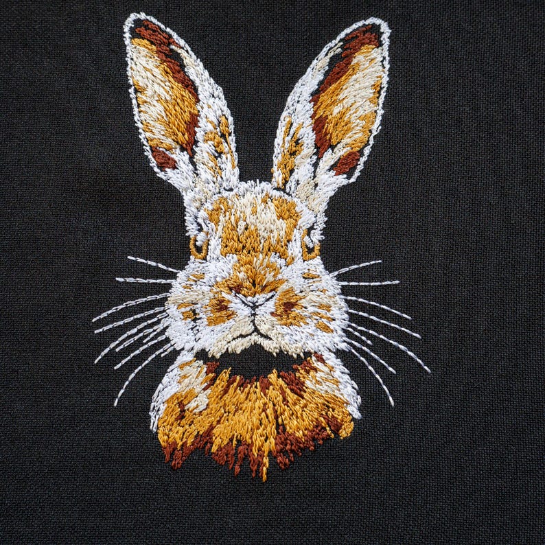 Peut inclure: Image brod&eacute;e d'un lapin brun avec du pelage blanc sur le visage et la poitrine. Le lapin a de longues oreilles et des moustaches. Le fond est noir.