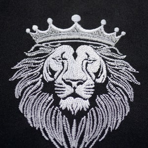 May include: White embroidered lion's head wearing a crown, set against a black backdrop. The detailed embroidery highlights the lion's mane and crown. The image is a close-up, emphasizing the texture and design of the embroidery.