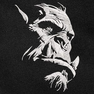 May include: Embroidered design of a fierce, stylized orc face in white thread on a black background. The orc has a large nose ring, tusks, and detailed facial features. The design is likely for apparel or accessories.